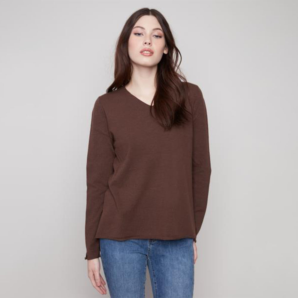 Woman wearing a brown long-sleeve top and blue jeans against a plain background