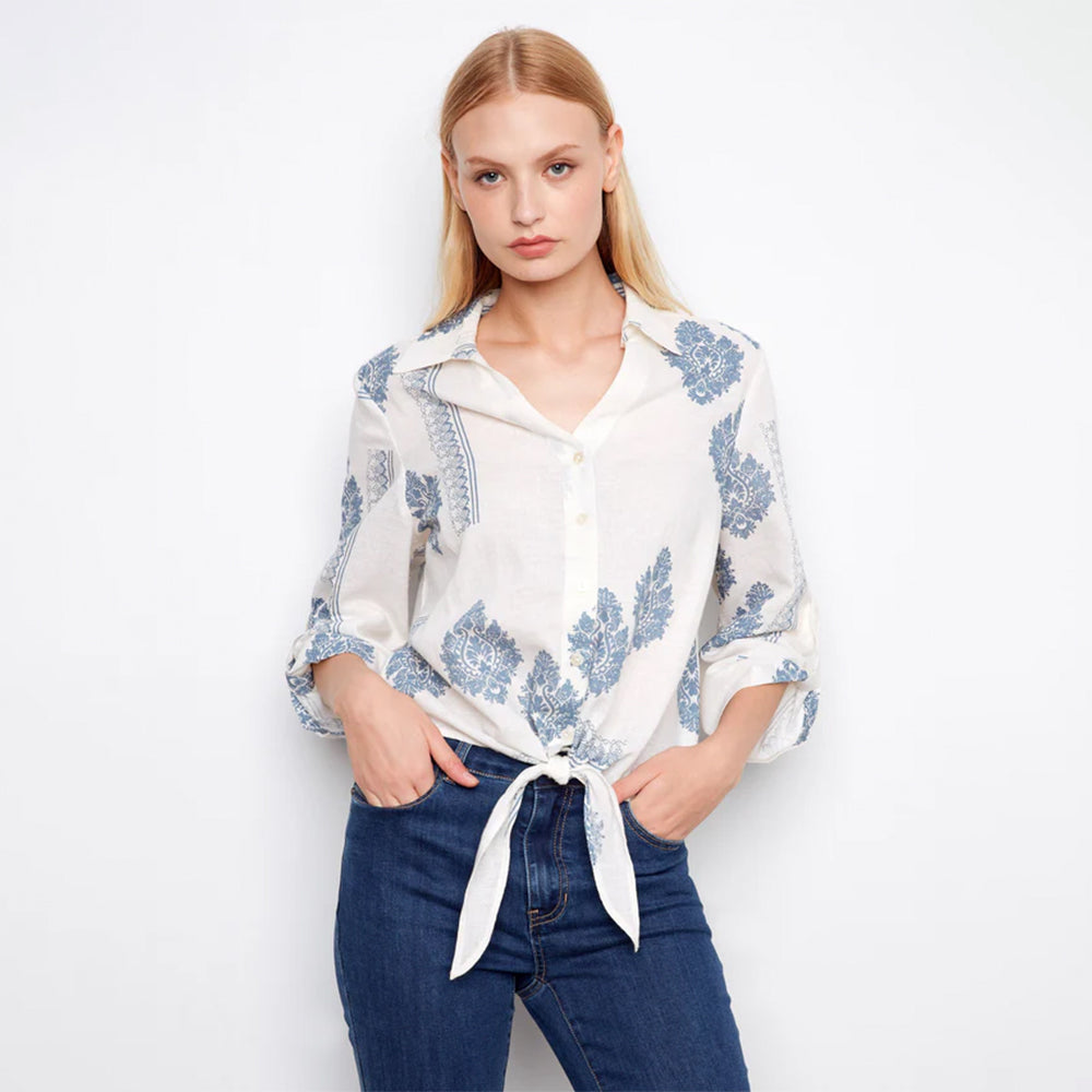 Woman wearing a white blouse with blue floral patterns and blue jeans on a white background