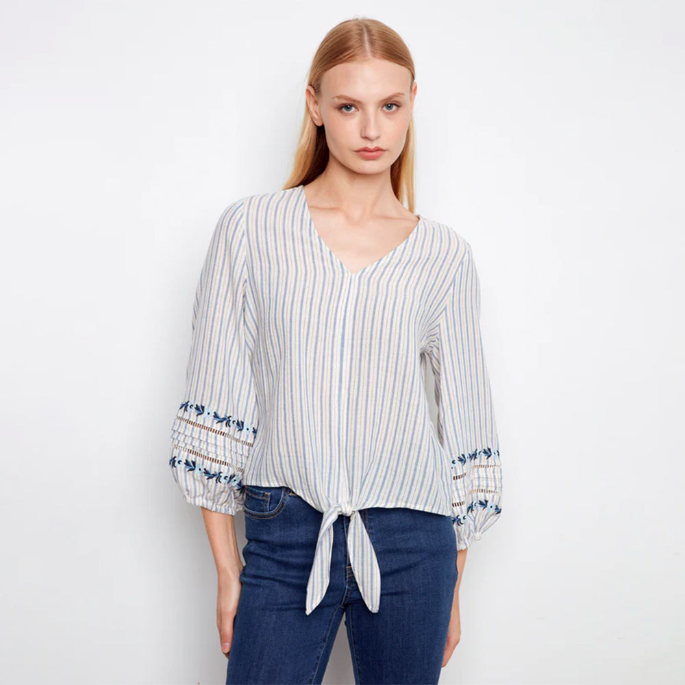 Woman wearing a striped blouse with blue accents and blue jeans on a white background