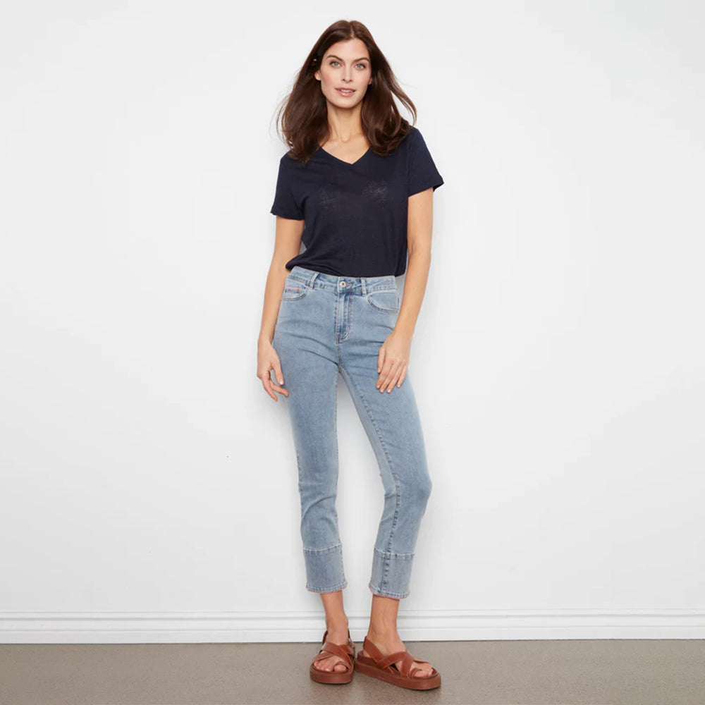 Woman wearing a navy t-shirt and light blue jeans against a white wall.
