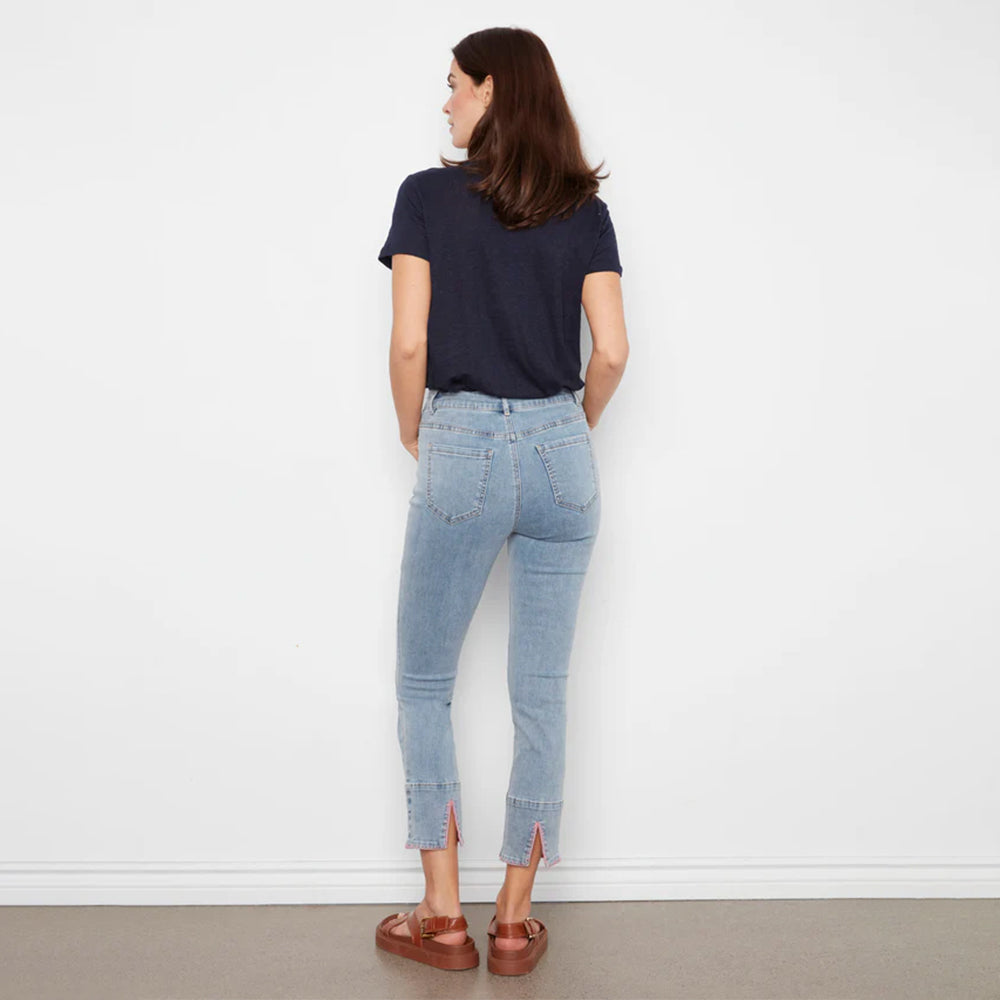 Woman wearing light blue jeans and a dark blue shirt against a white wall.