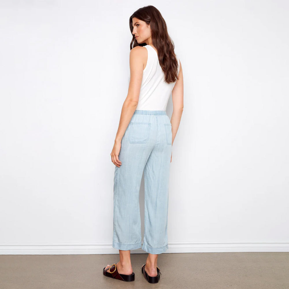 Woman wearing light blue pants and a white top against a plain background