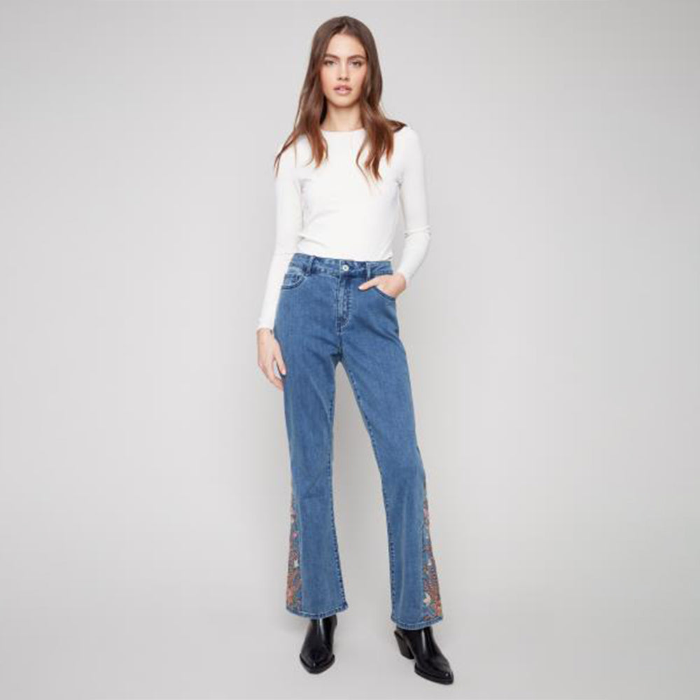 Woman wearing blue jeans with floral hem on a gray background