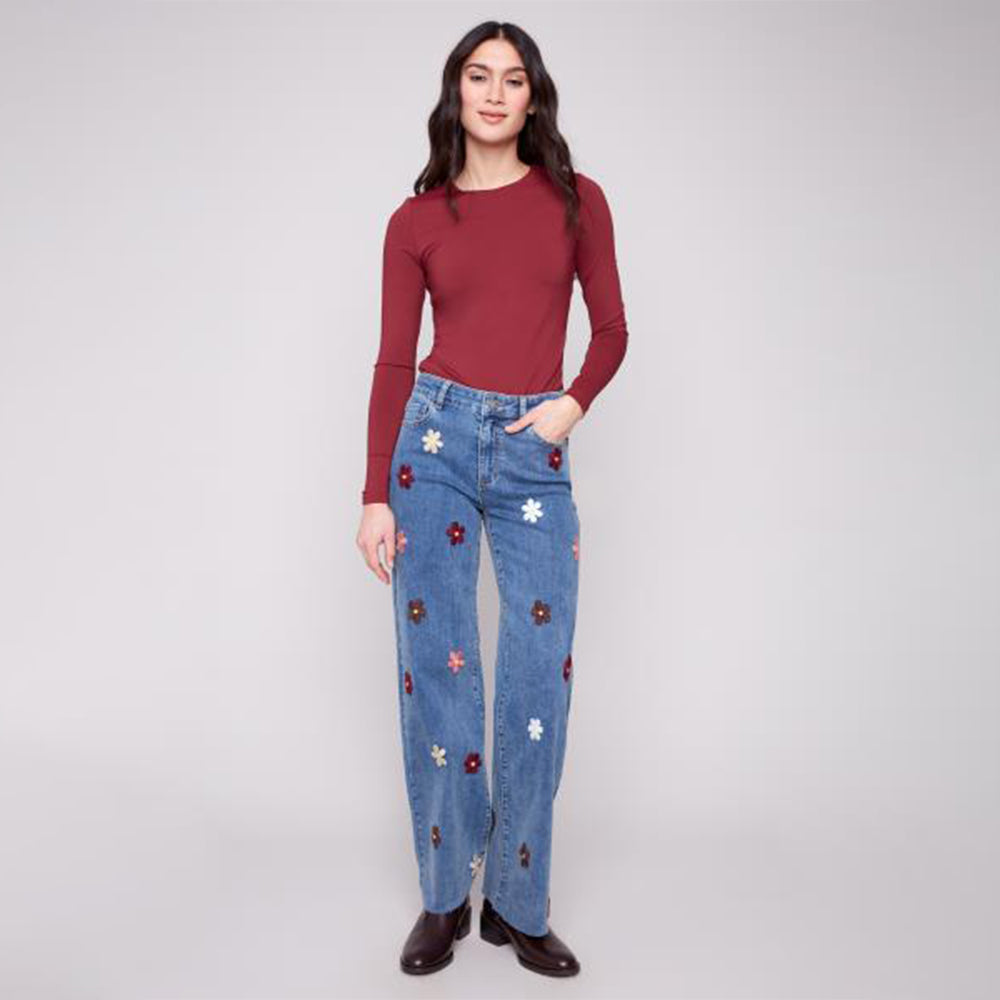 Woman wearing blue jeans with floral embellishments and a red top on a white background
