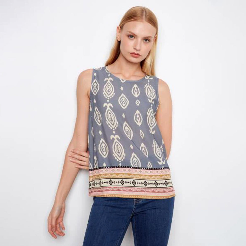 Woman wearing a sleeveless patterned top and jeans on a white background