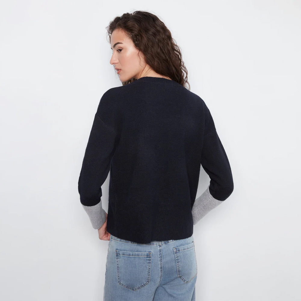 A woman shown from the back wearing a dark navy knit sweater with light gray ribbed cuffs, paired with light blue jeans, against a plain white background.