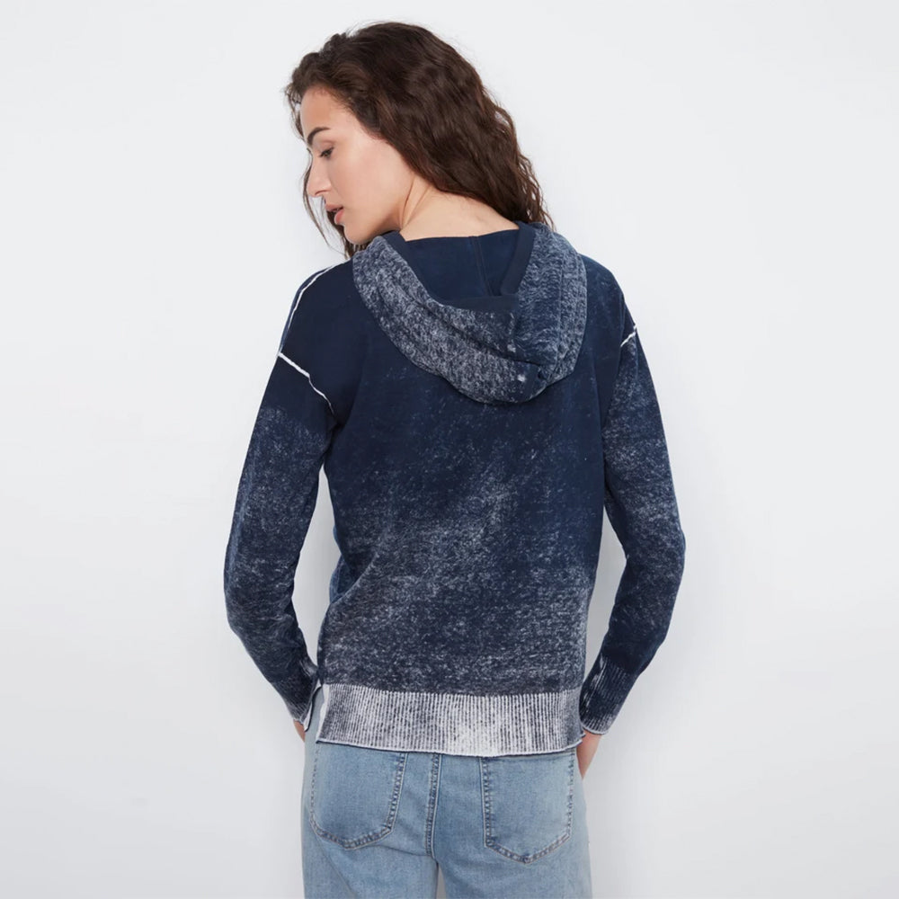 A woman shown from the back wearing a dark navy hooded sweatshirt with a marbled lighter blue-gray texture, paired with light blue jeans, against a plain white studio background.