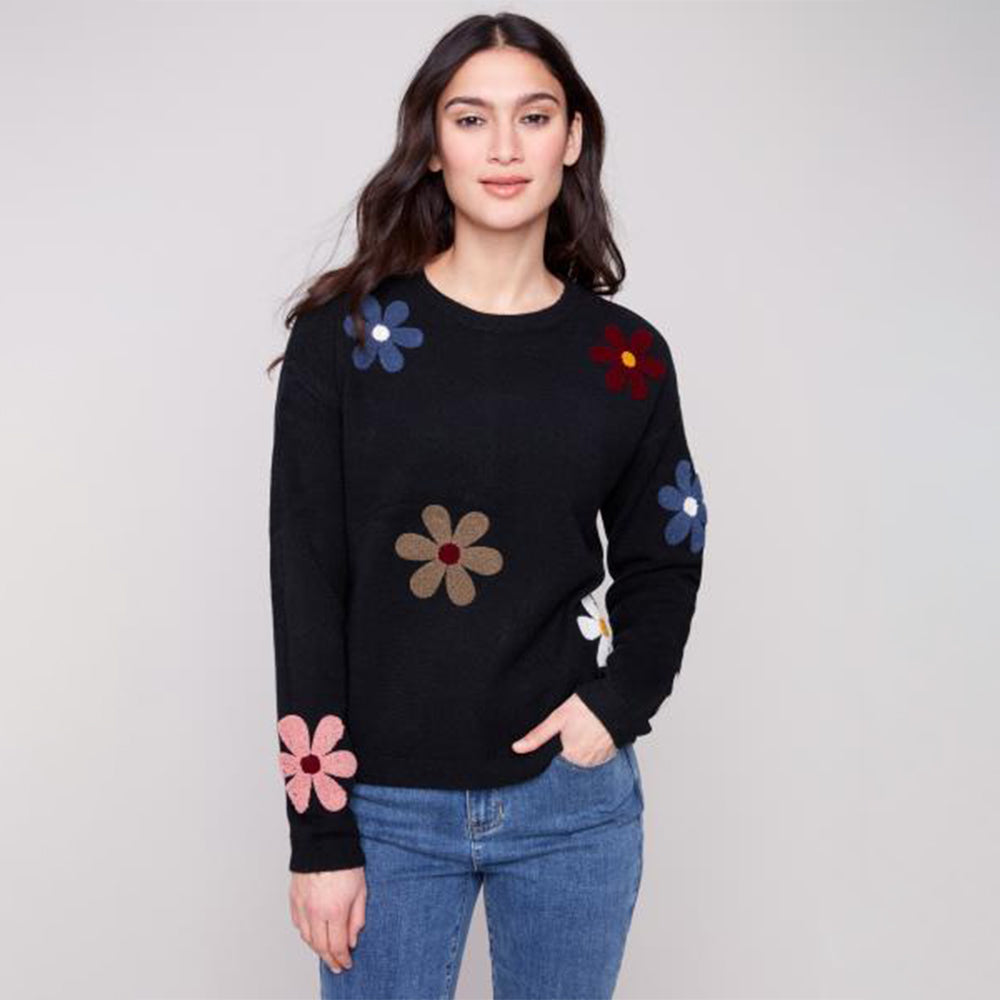 Woman wearing a black sweater with colorful flower patterns on a gray background
