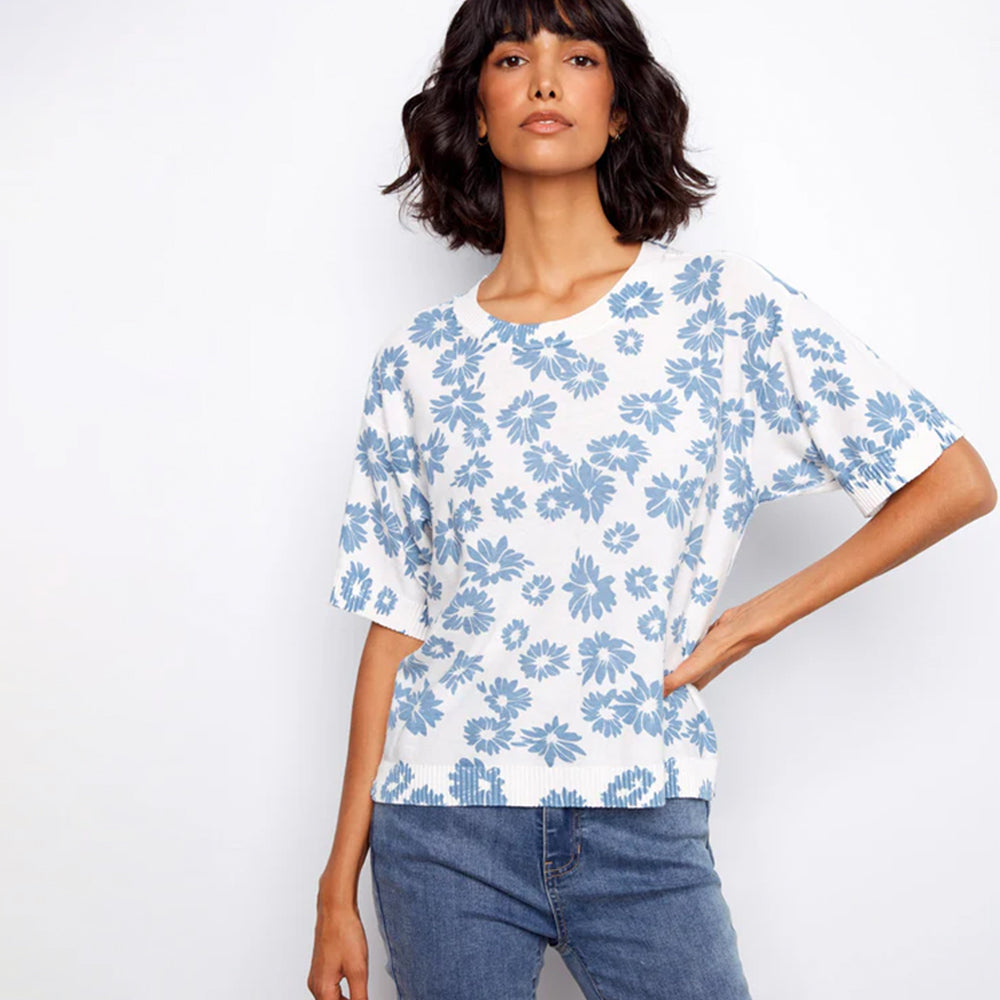 Woman wearing a white blouse with blue floral pattern and blue jeans on a white background