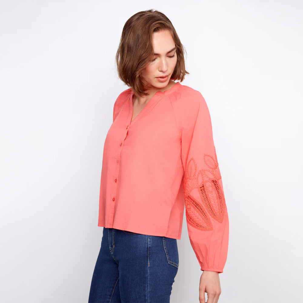 Person wearing a coral long-sleeve top with lace details on a white background