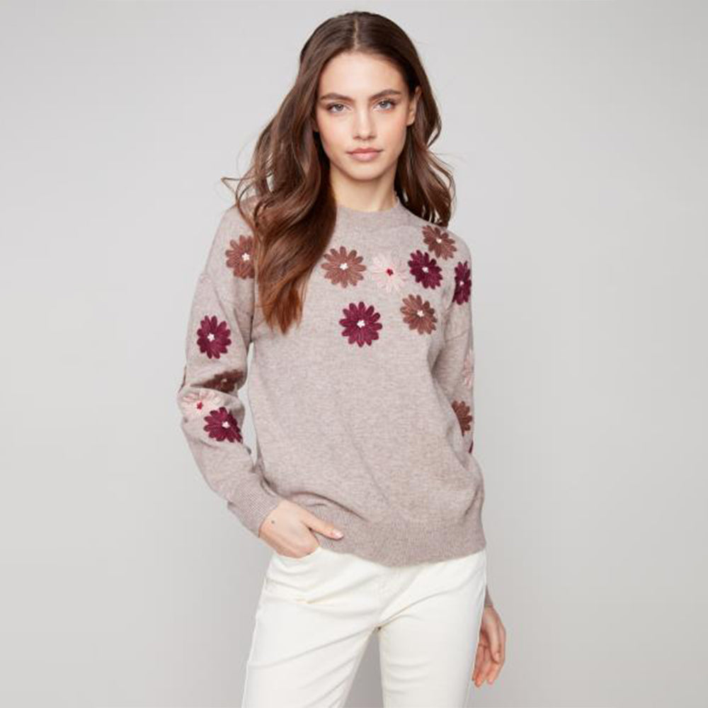 Woman wearing a gray sweater with floral patterns on a plain background