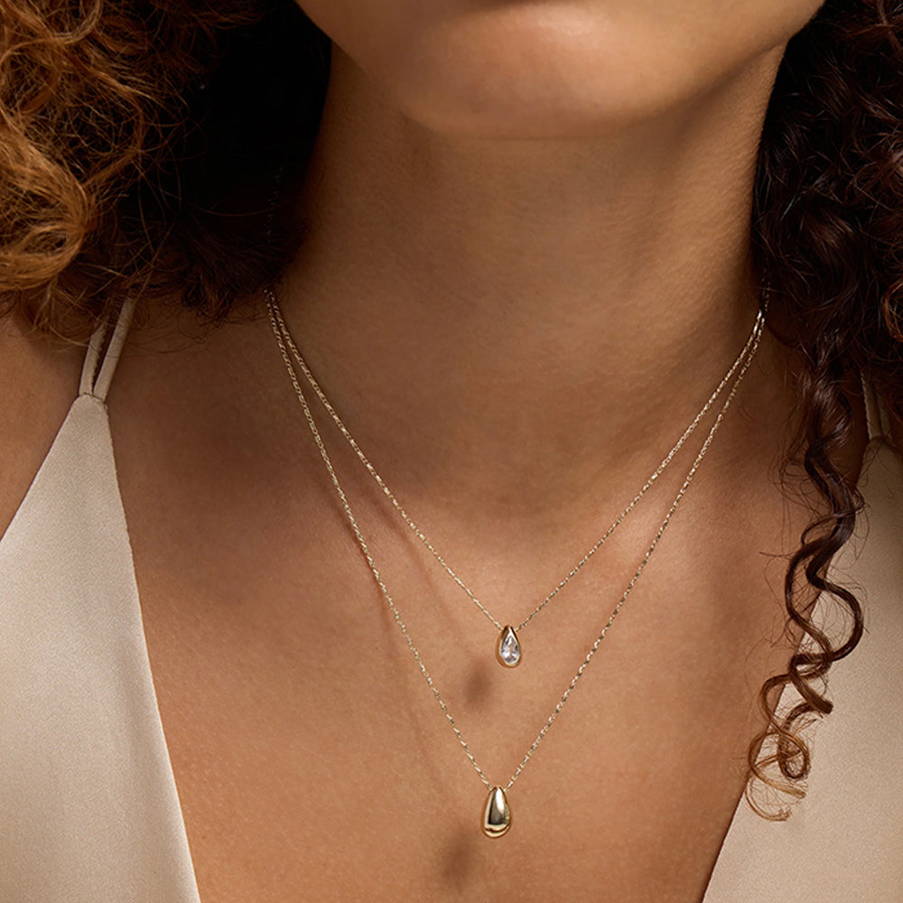 Two silver teardrop pendant necklaces on delicate chains, around a woman's neck