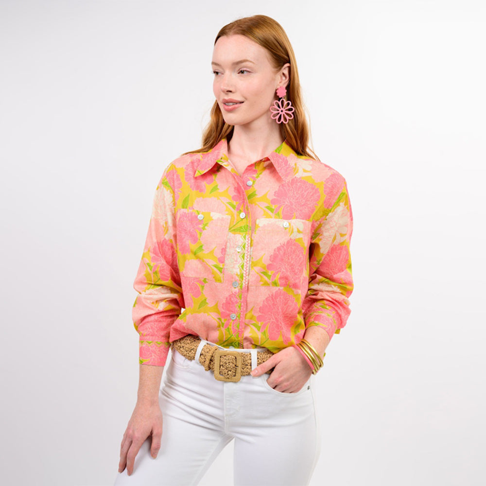 Woman wearing a pink floral blouse and white pants on a plain background