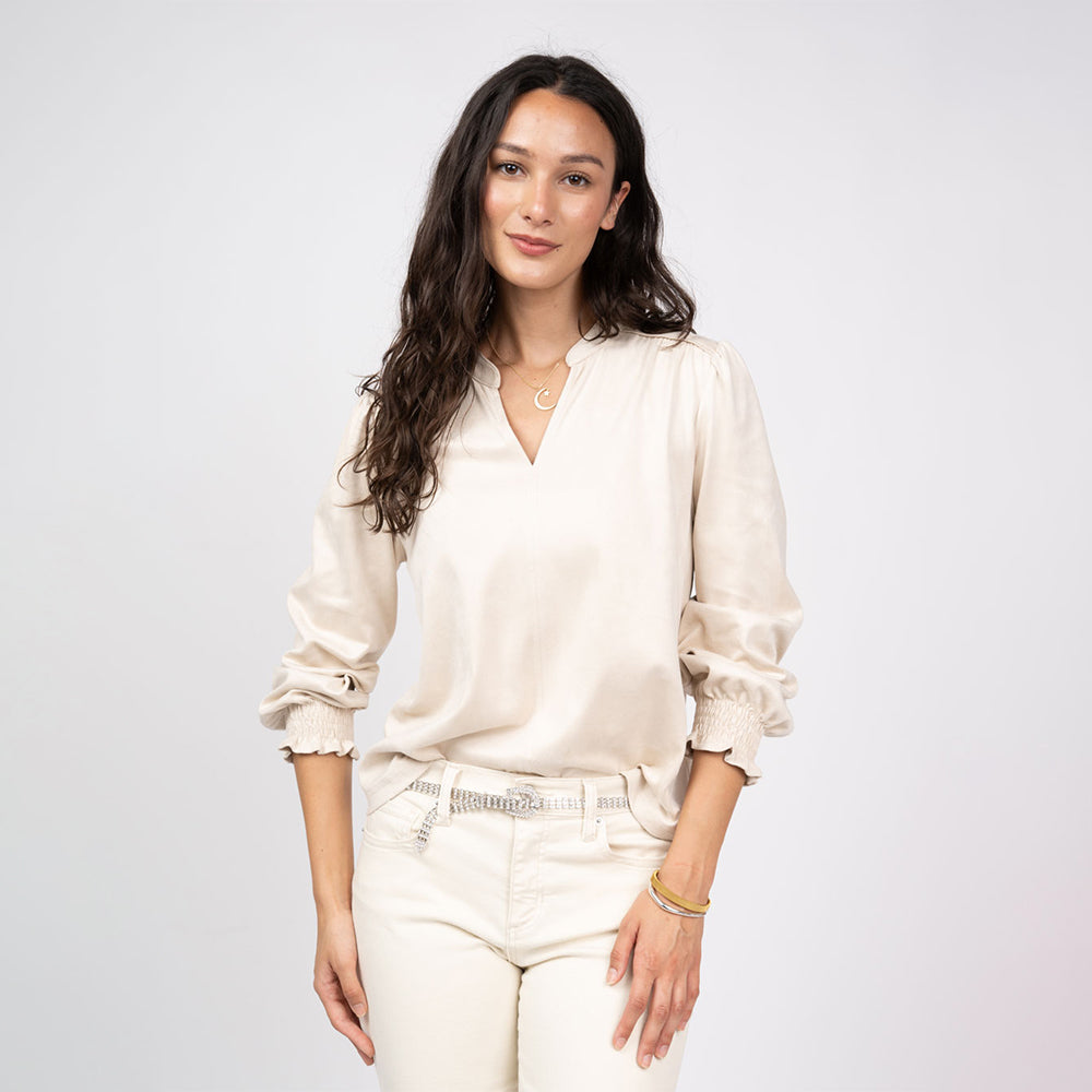 Woman wearing a beige blouse and white pants against a plain background