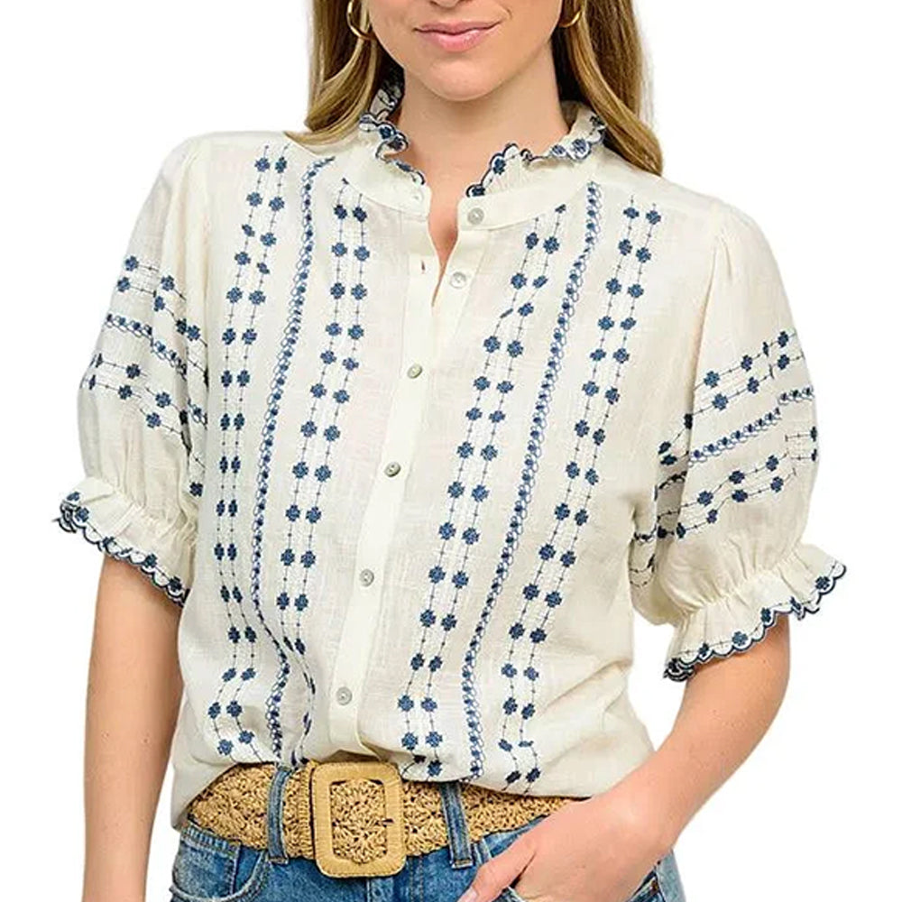 Woman wearing a white blouse with blue floral patterns and rolled-up sleeves, standing against a white background.
