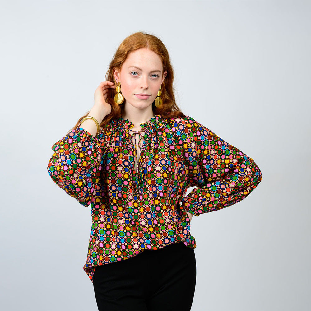 Woman wearing a colorful patterned blouse against a plain background