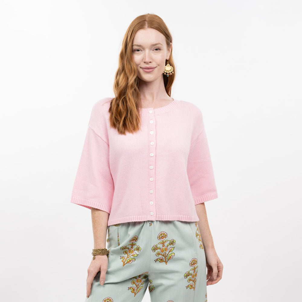 Woman wearing a pink cardigan and light blue pants with floral embroidery on a white background