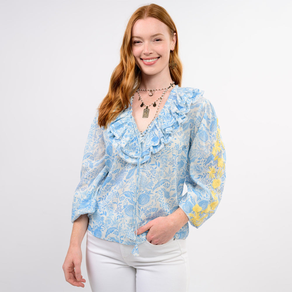 Woman wearing a blue floral blouse with ruffled details on a white background