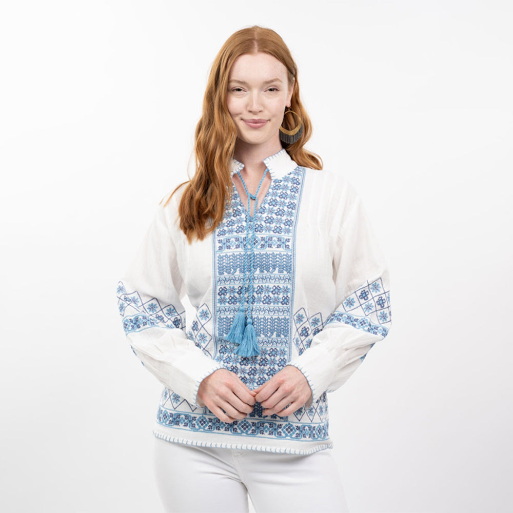 Woman wearing a white blouse with blue embroidery on a white background