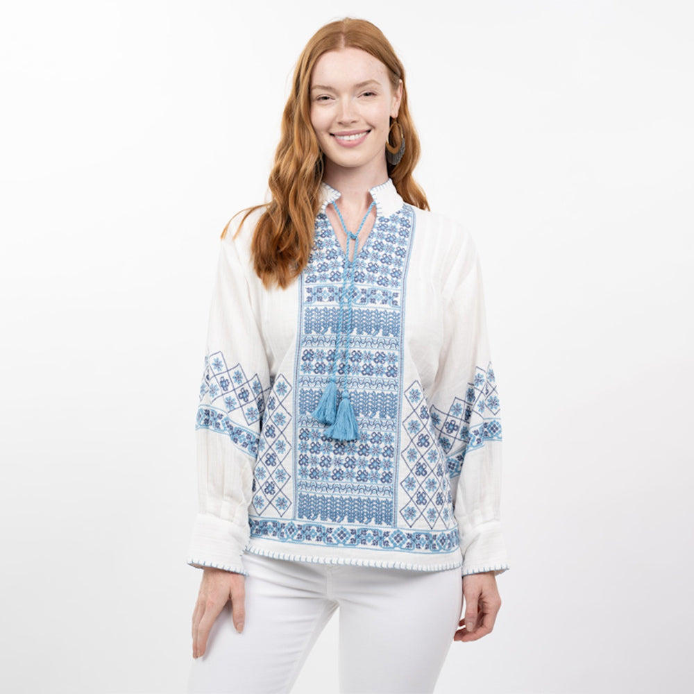 Woman wearing a white blouse with blue embroidery on a white background