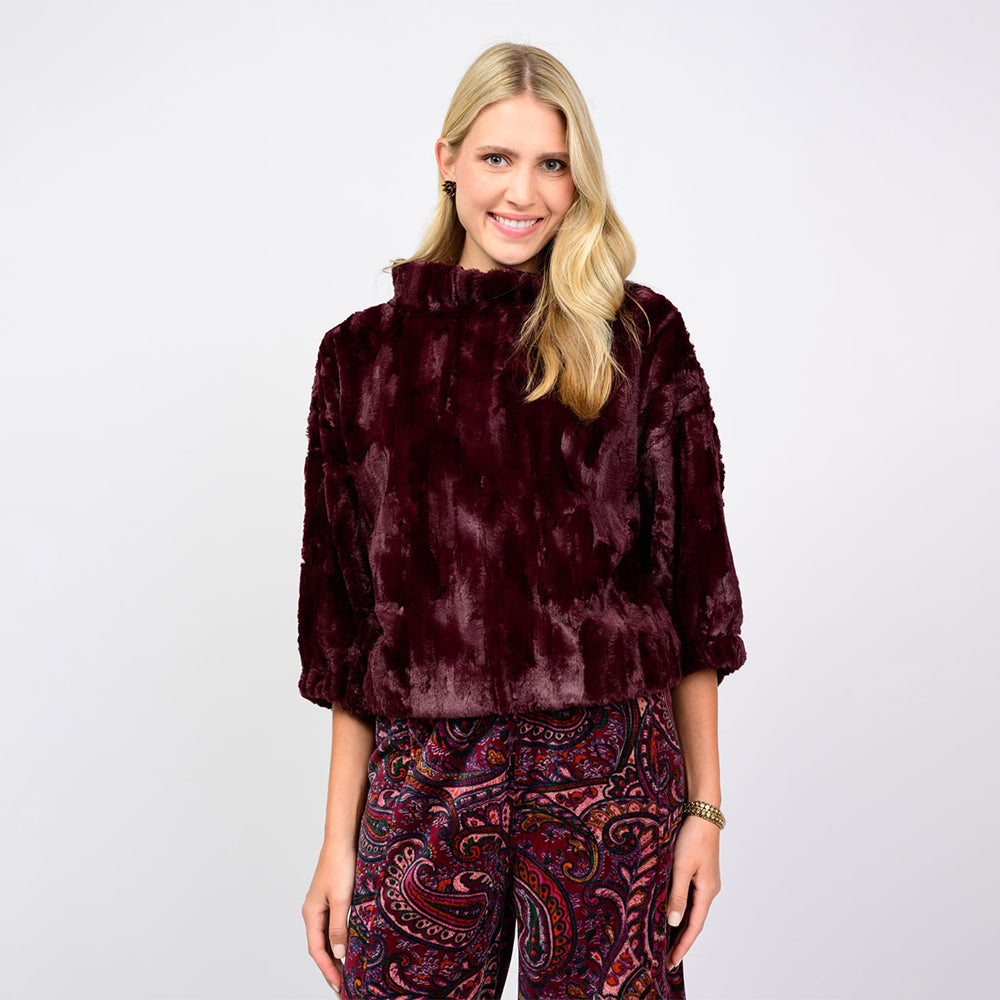 Woman wearing a burgundy textured top and paisley pants on a white background