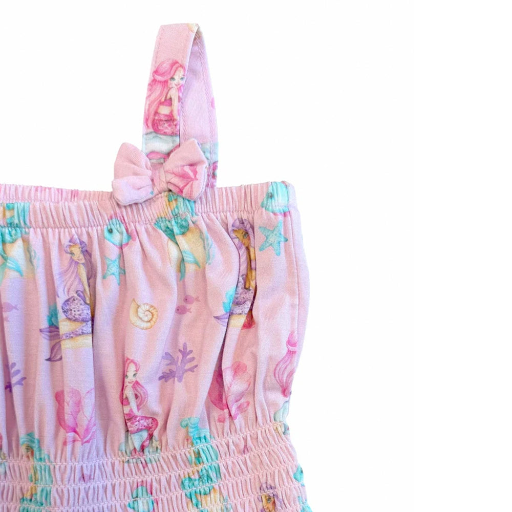 A close-up of a pink fabric garment featuring a mermaid and sea life print, with a matching pink bow detail on the shoulder strap, set against a plain white background.