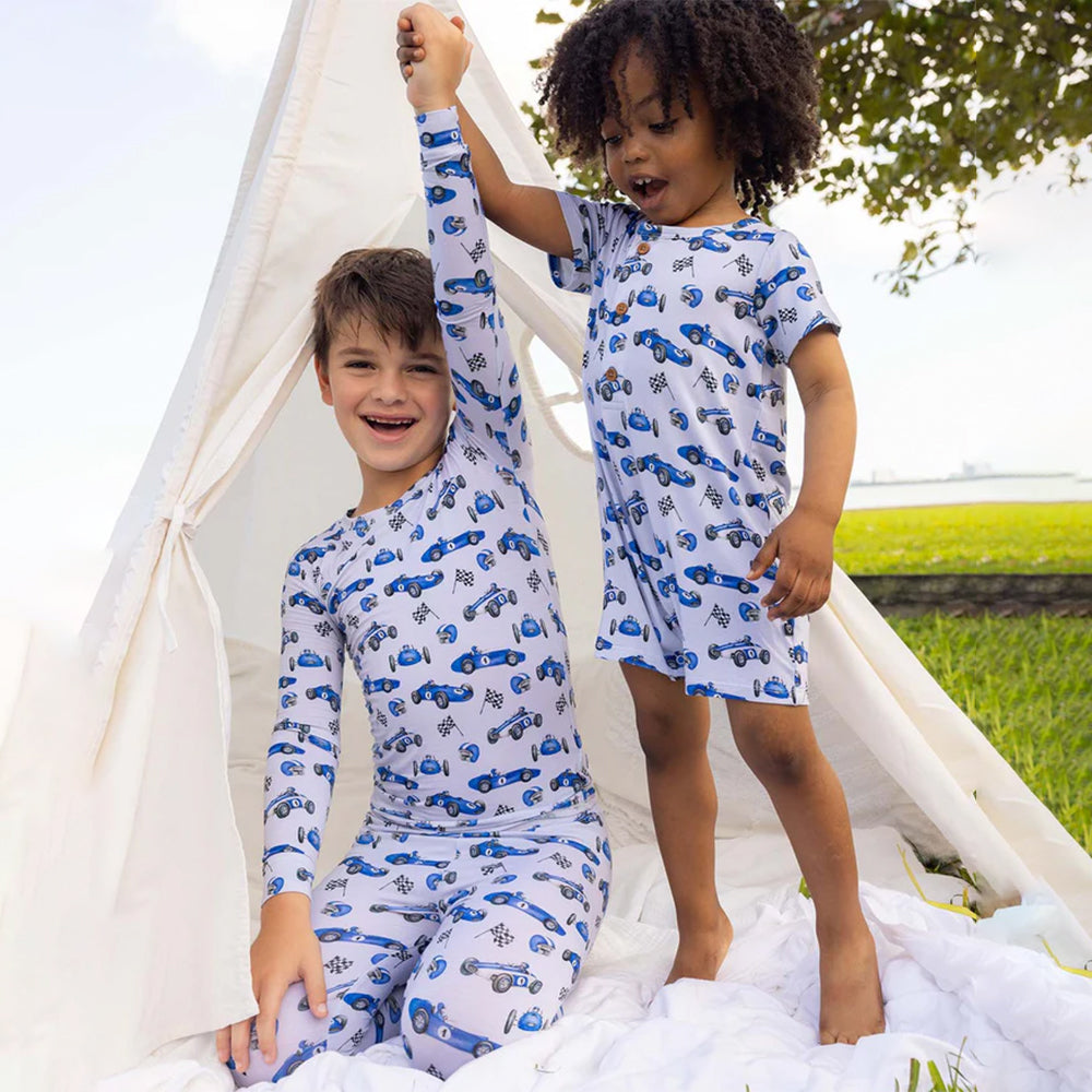 Two children in matching blue and white pajamas with car pattern standing inside a white teepee.