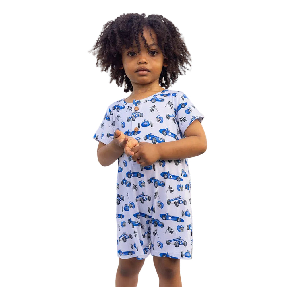 Child wearing a blue and white car-patterned dress standing in front of a white tent.