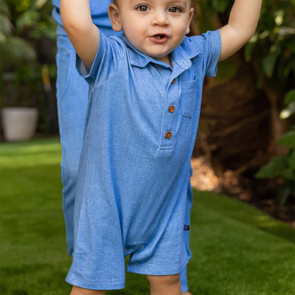 Child wearing a blue outfit with buttons outdoors on grass