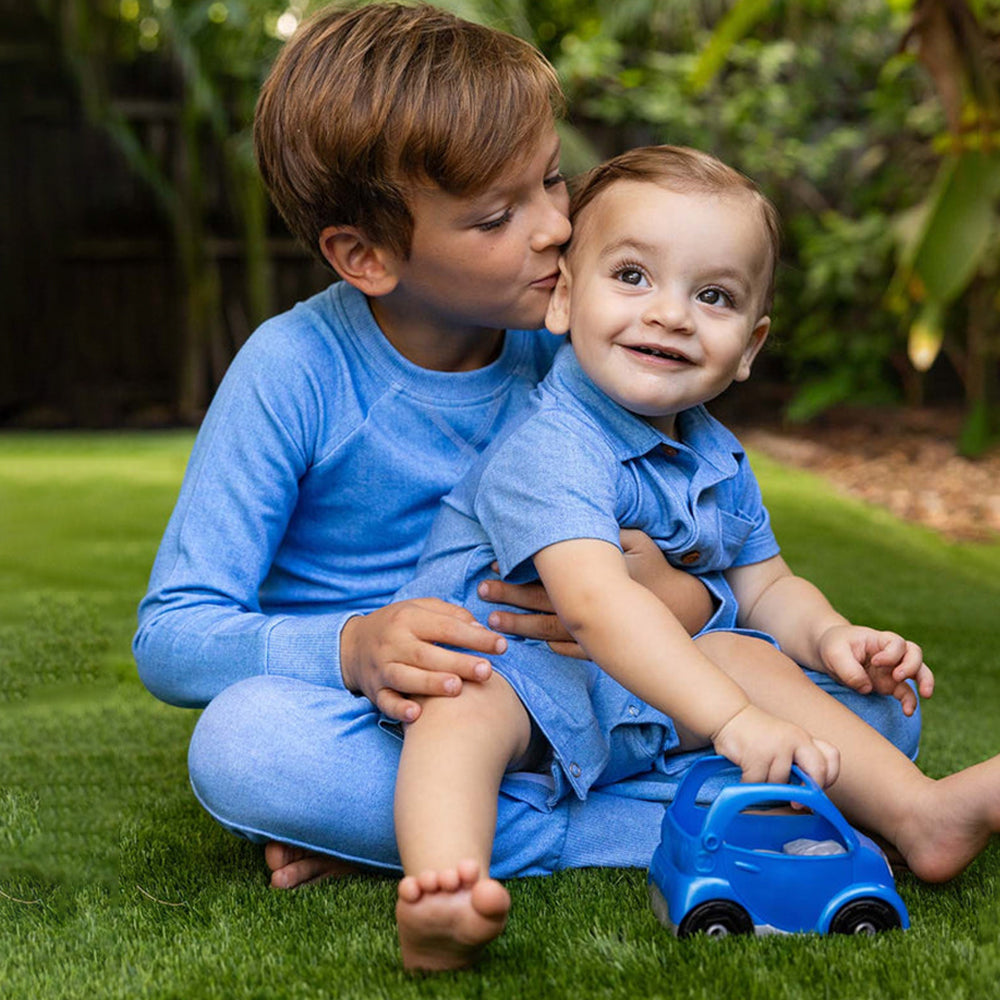 Two children in blue outfits playing with a toy car on grass