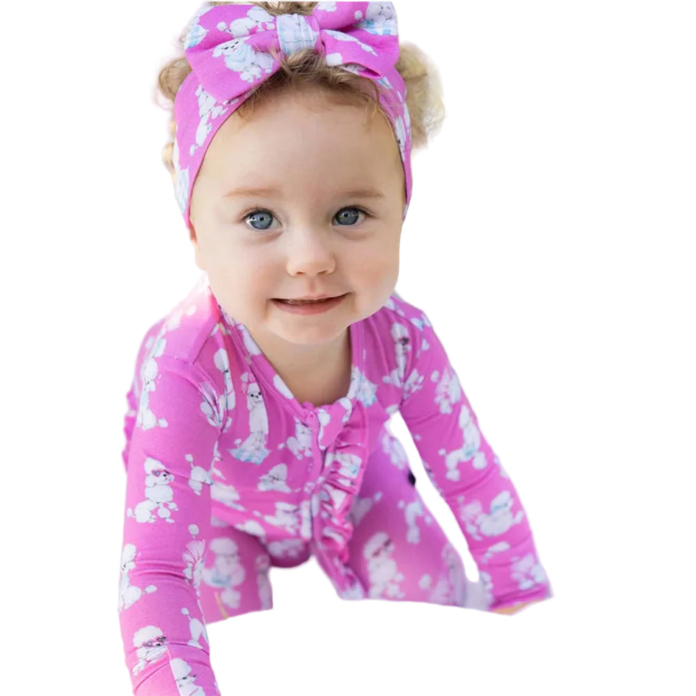Baby wearing a pink outfit with cloud pattern and matching headband, sitting outdoors.