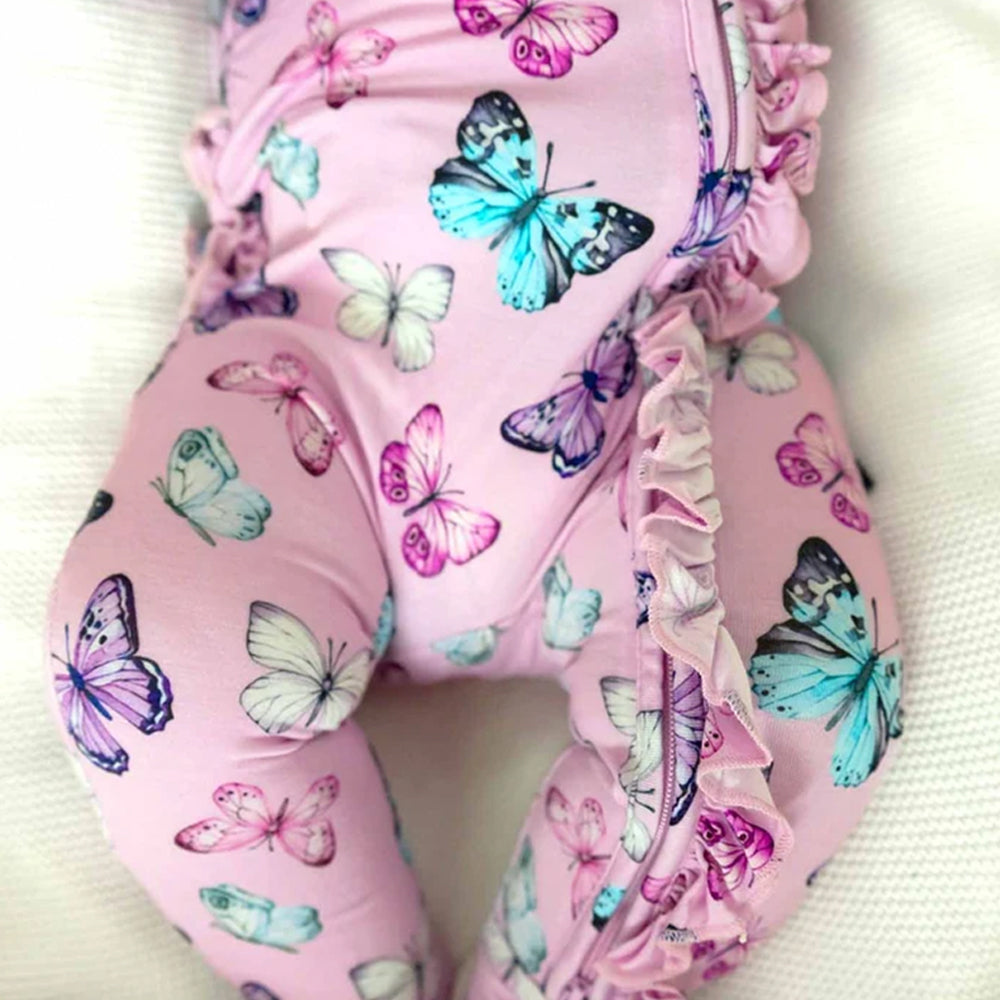 Pink baby leggings with a colorful butterfly print and ruffled trim, shown on a baby lying on a textured white blanket.