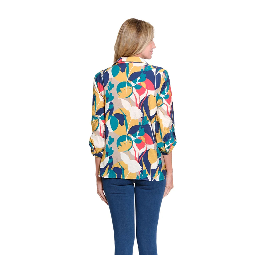 A woman viewed from the back wearing a long-sleeve button-up shirt with a colorful abstract floral pattern in yellow, teal, navy, pink, and cream, paired with dark blue jeans against a plain white background.
