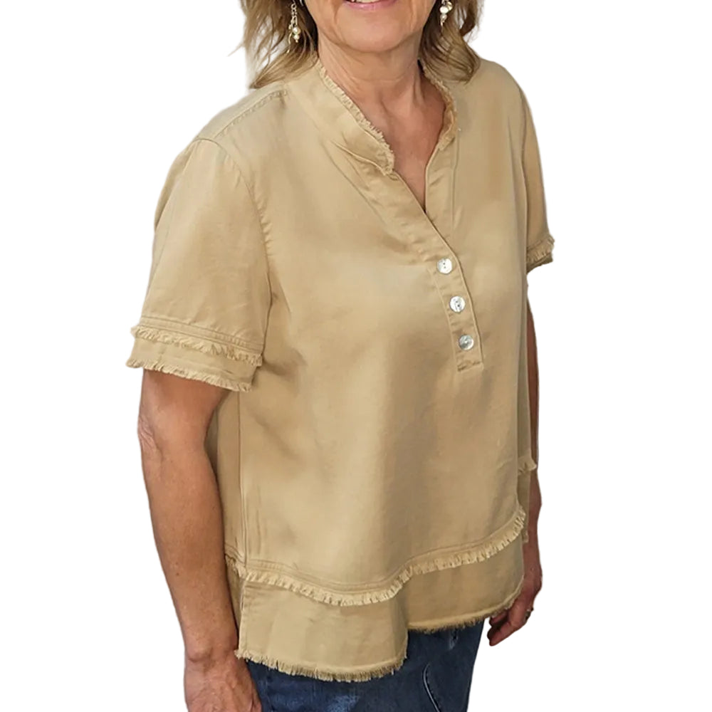 Woman wearing a beige blouse with button details against a stone wall.