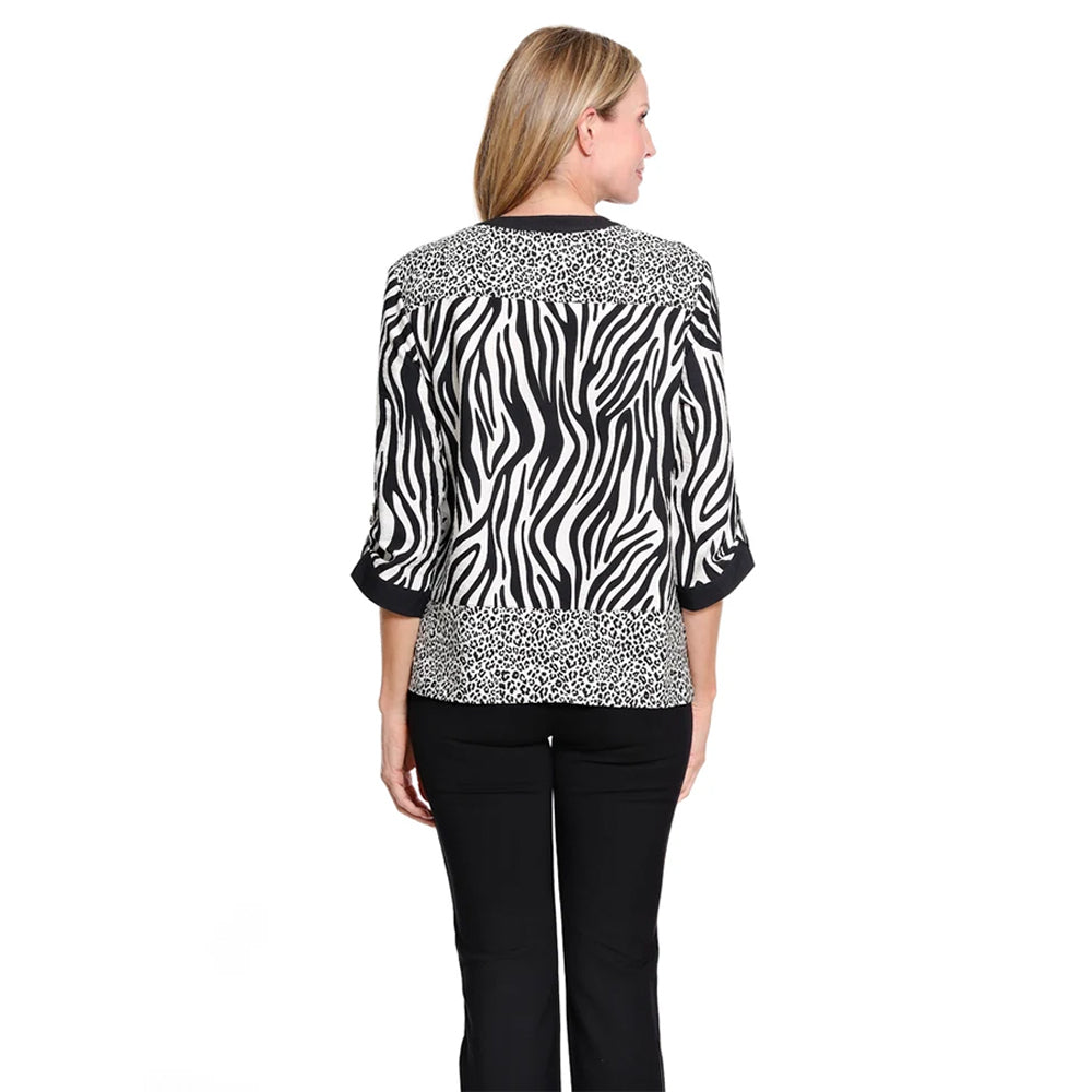 A woman modeling a black and white zebra-print button-up blouse with leopard-print patterned cuffs and hem, paired with black pants, against a plain white background.
