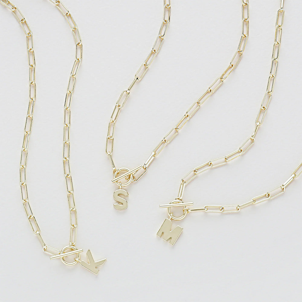Three gold chain necklaces with charms on a light gray background