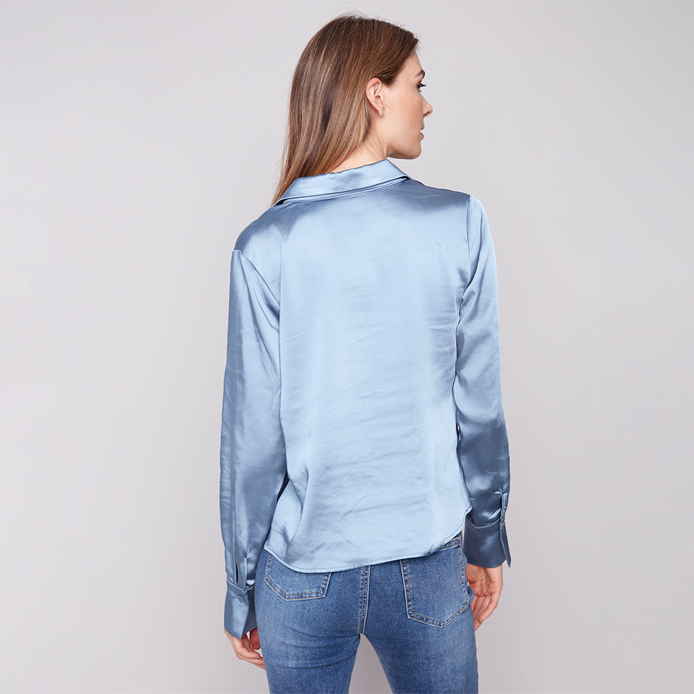 Woman wearing a light blue satin shirt and jeans on a plain background