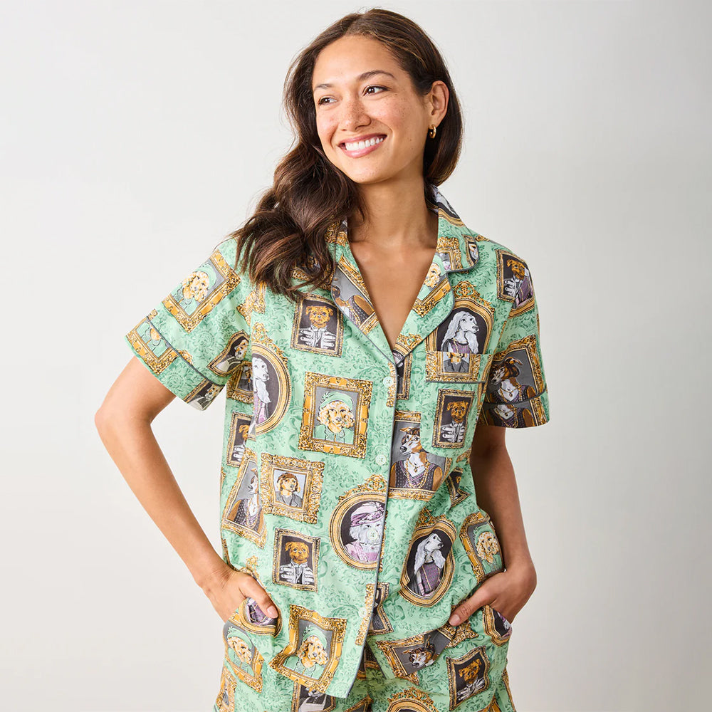 Woman wearing a green patterned shirt with portrait designs on a plain background