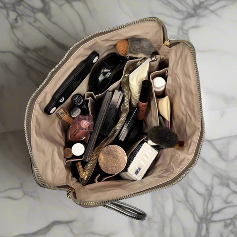 Open makeup bag with various cosmetic items on a marble surface