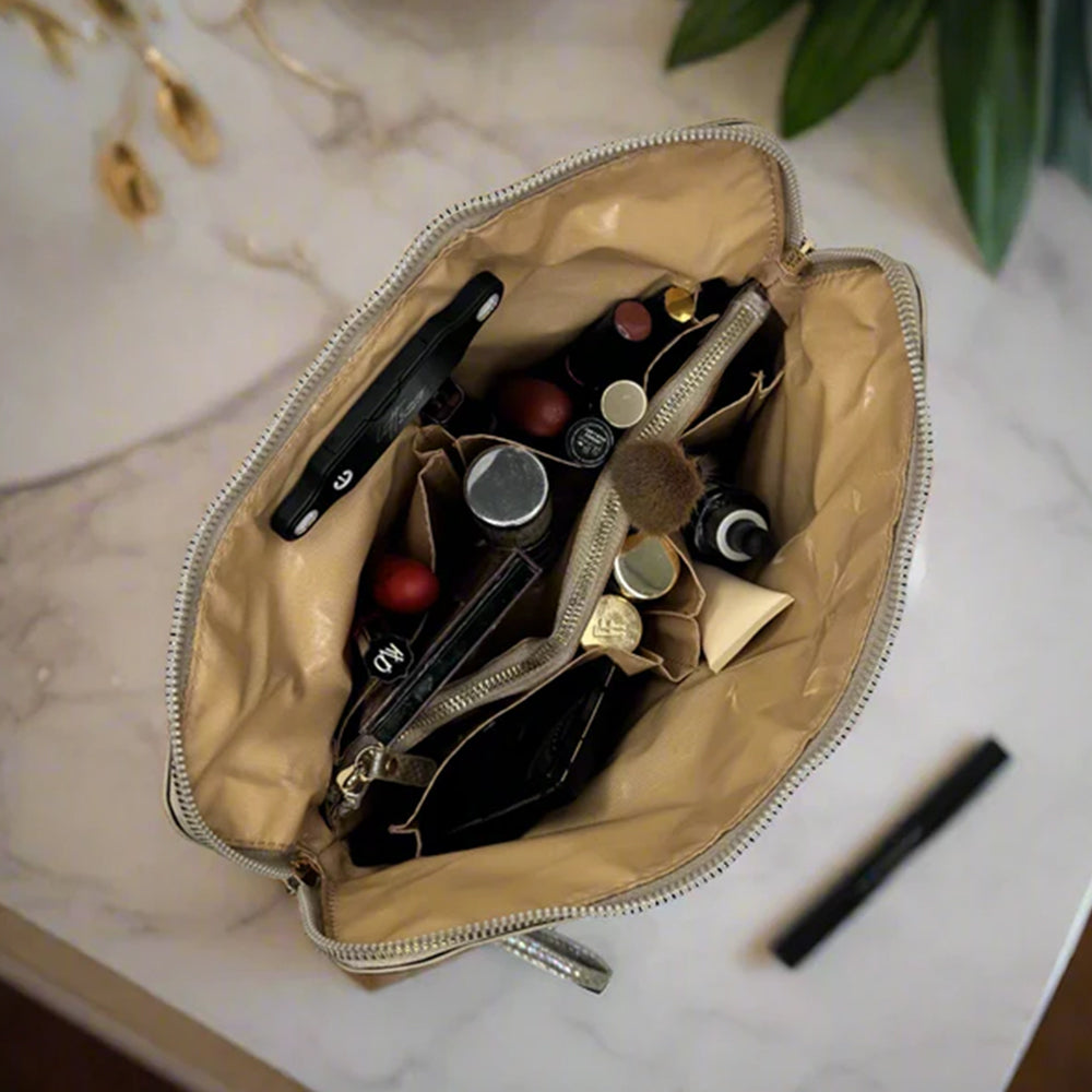 Open beige makeup bag with various cosmetic items on a marble surface