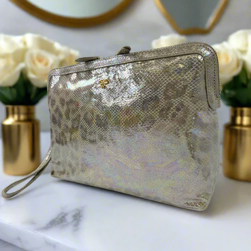 Silver metallic clutch bag on a marble surface with floral arrangements in the background