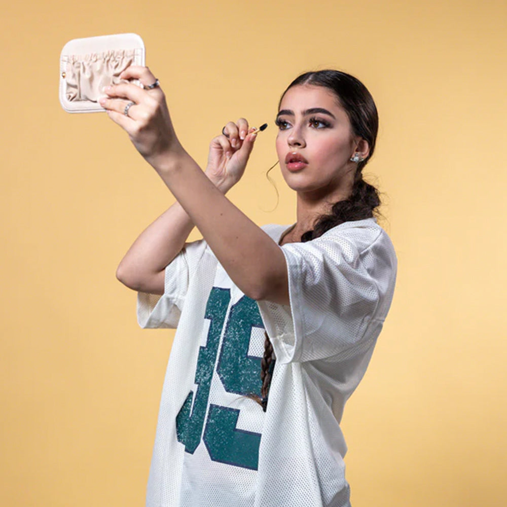 Woman applying makeup in front of a mirror on a beige background