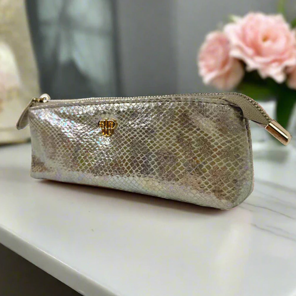 Gold glittery pouch with a gold zipper on a white surface with pink flowers in the background