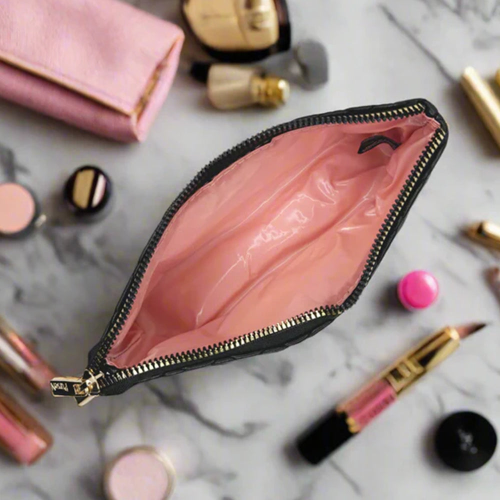 Open black makeup pouch with pink interior on a marble surface with cosmetics.