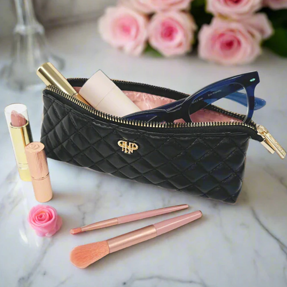 Black quilted makeup bag with cosmetic items on a marble surface with pink roses in the background