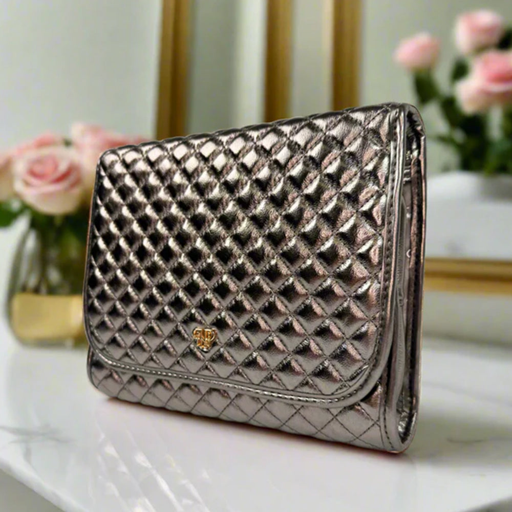 Quilted clutch bag with a brand logo on a white surface with flowers in the background