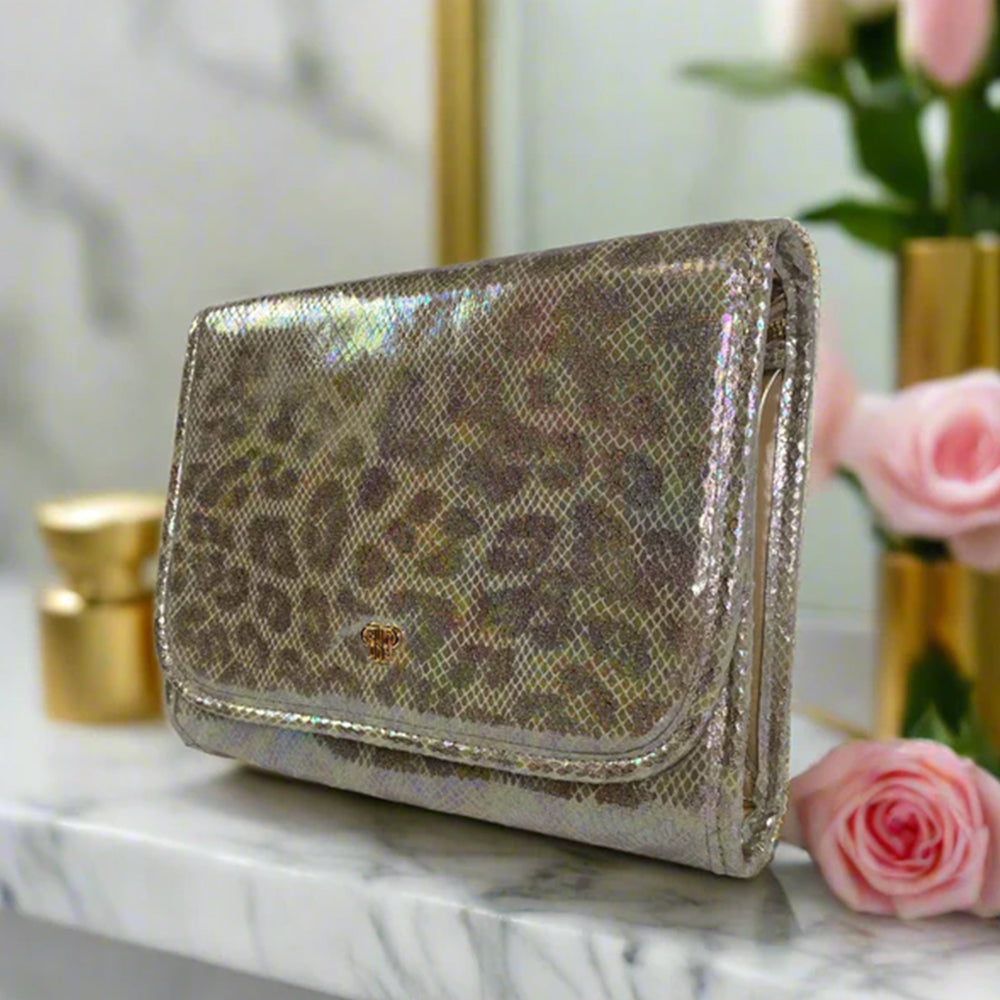 Gold metallic leopard print wallet on a marble surface with flowers and candles in the background