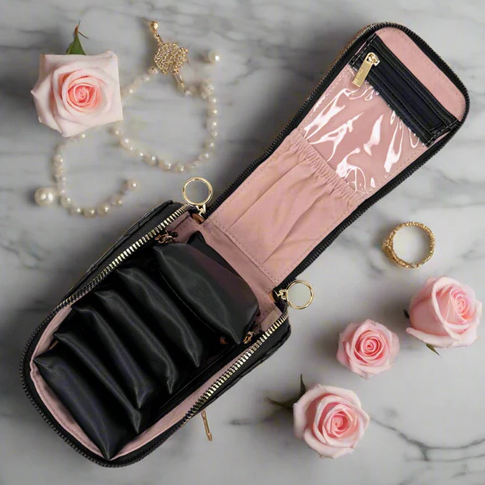 Pink jewelry case with black interior compartments on a marble surface with pink roses and gold jewelry.