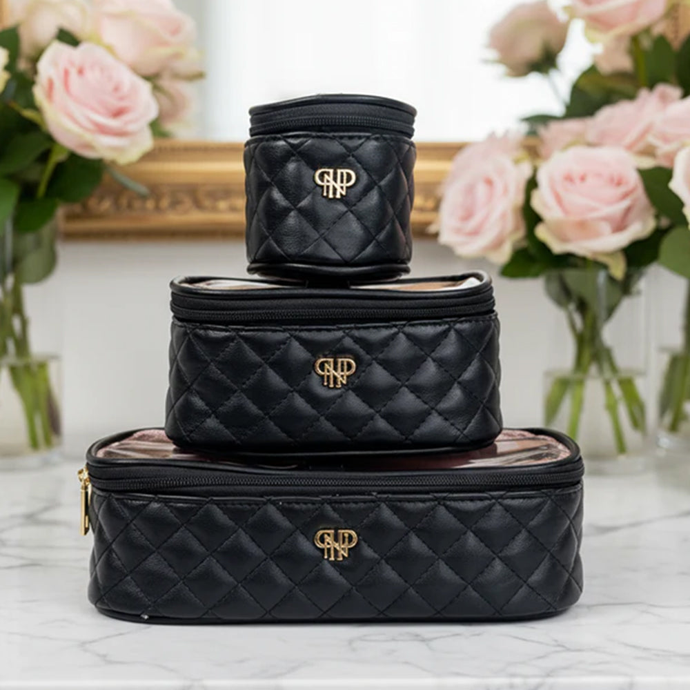 Stack of black quilted cosmetic bags with a logo on a marble surface with flowers in the background