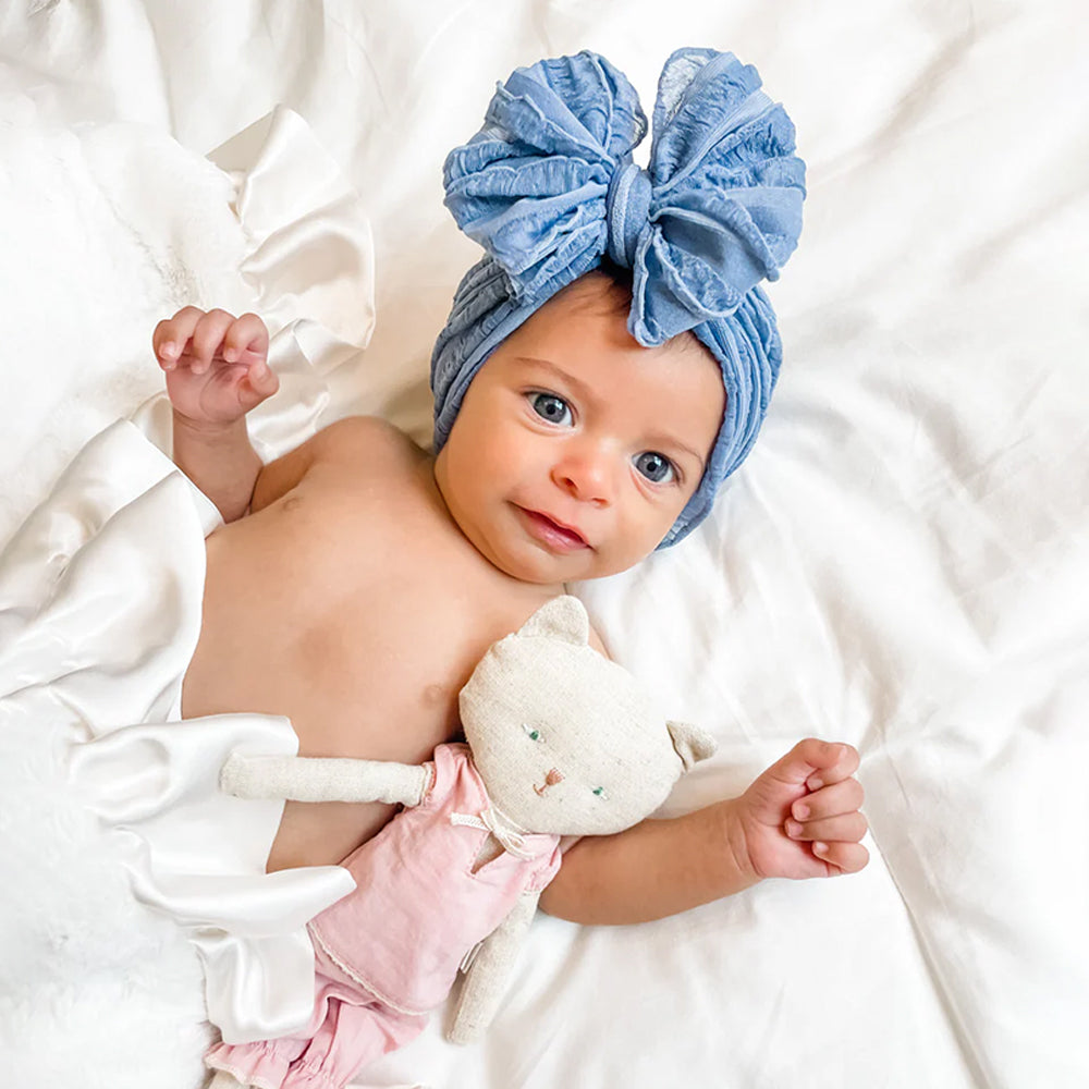 Baby wearing a blue headband with a bow, holding a white plush toy on a white background